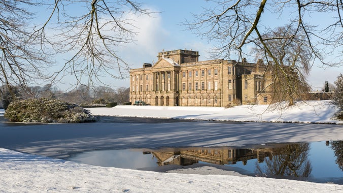 A view of Lyme house covered in snow. The house can be seen in the frozen reflection pond.